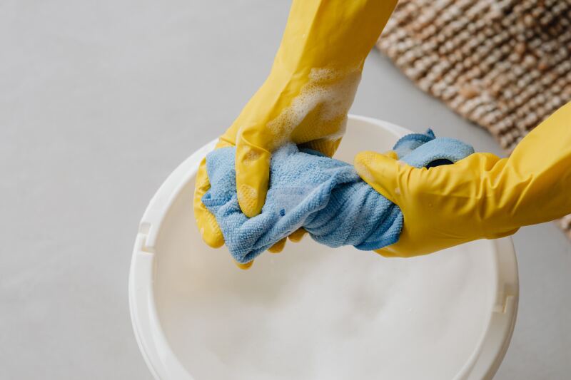 Hands in yellow gloves wringing out a blue towel over a bucket