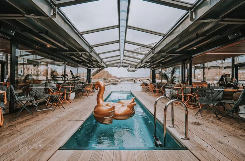 Narrow pool with large gold swam float, plus skylight above and wooden deck in floating hotel
