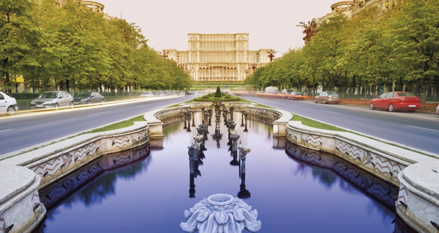 A large tiered building at the end of a fountain-lined roadway.