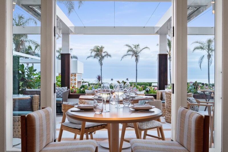 A table setting looking out onto an open patio and palm trees at Serẽa Restaurant, Hotel del Coronado, California.