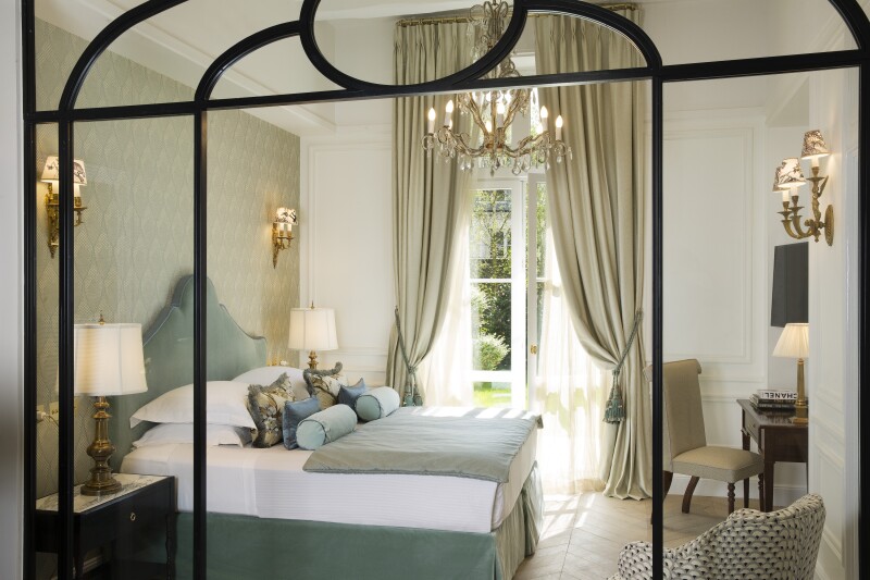 A Garden Suite, with ornate scones and chandelier, curtained glass doors opening to outdoors, and pale blue accents