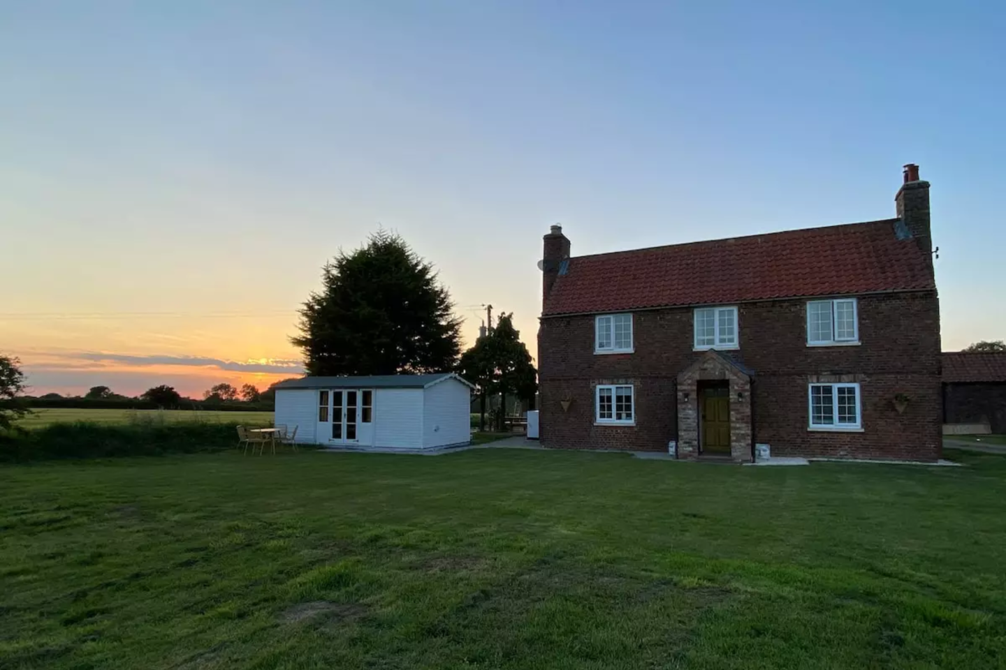 نمای بیرونی یک خانه دو طبقه آجری در مزرعه هنگام غروب آفتاب