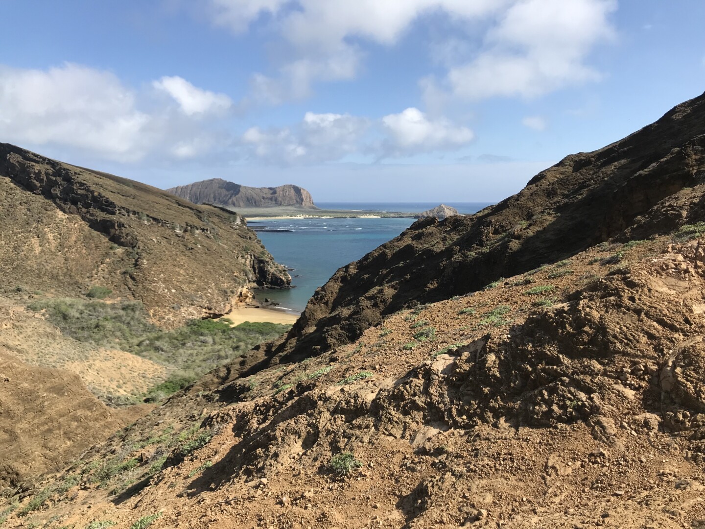 Rocky valley leading down to a sandy beach, overlooking ocean with mountains in distance