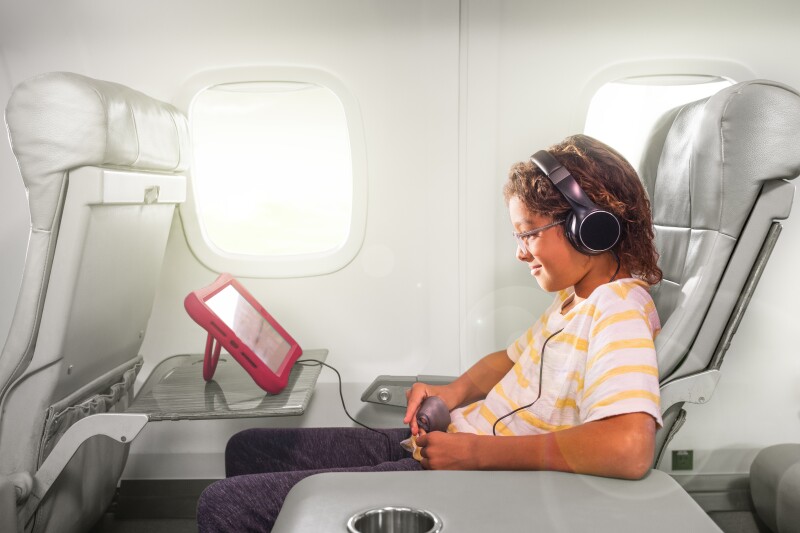A young passenger on a JSX flight wears headphones and looks at an iPad