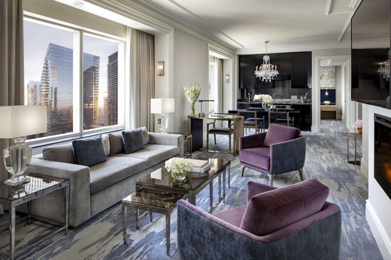 Two-bedroom suite, with long sofa under windows, violet-colored armchairs, and abstract patterned carpet