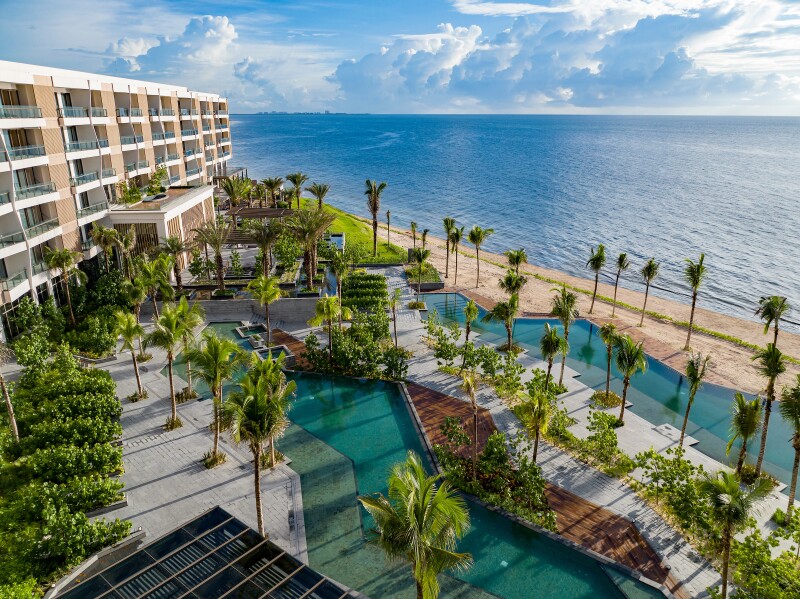 Aerial view of the Waldorf Astoria Cancun next to the ocean, with two long asymmetrical pools and palm trees.