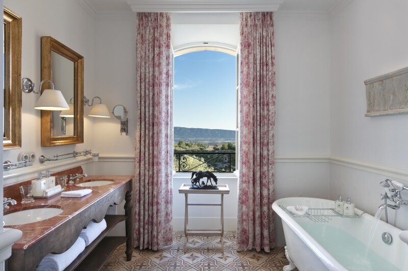 The enormous bathrooms at La Bastide de Gordes include double sinks, a white clawfoot tub, and views of the Provencal countryside.