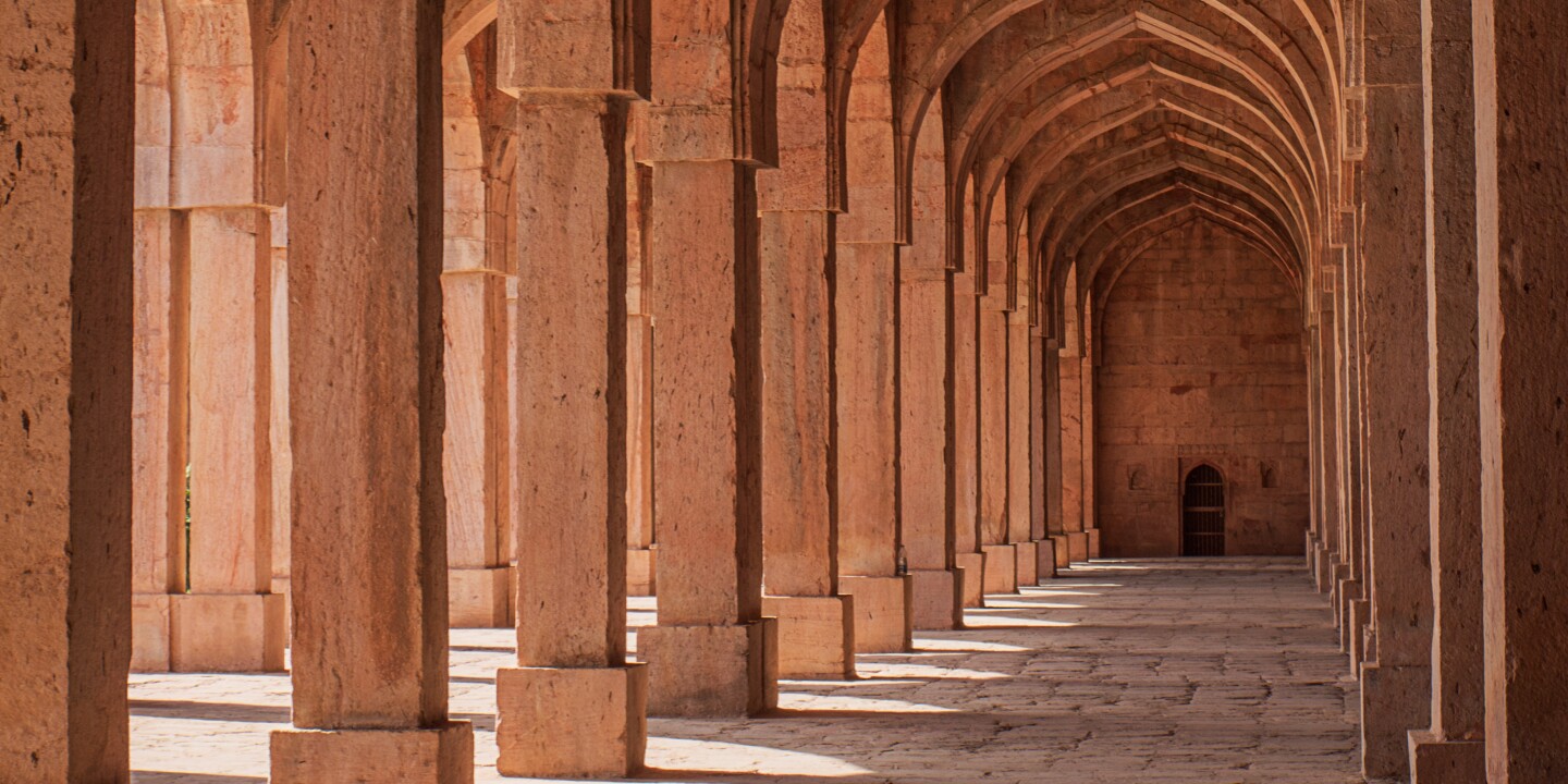 Interior of loggia in red sandstone mosque with arches and shadows and sunlight
