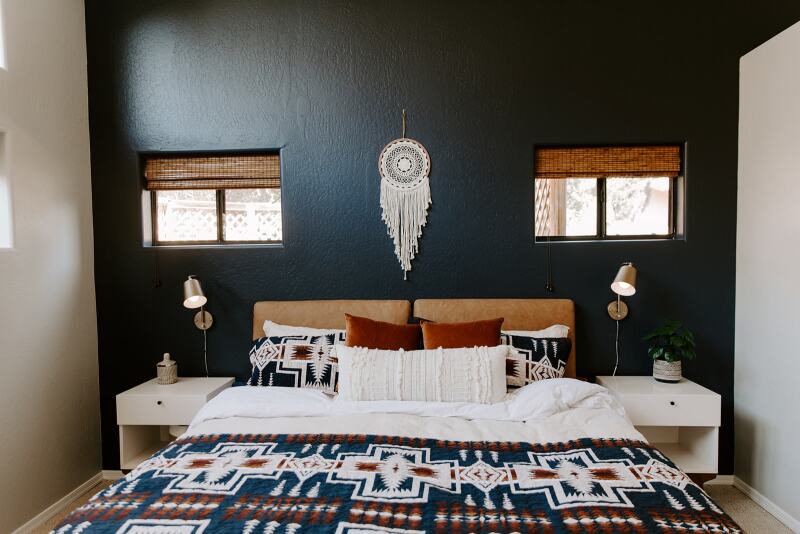 Large bed with a Native American–inspired textile, under a white yarn dreamcatcher, backed by a navy blue wall with two small windows