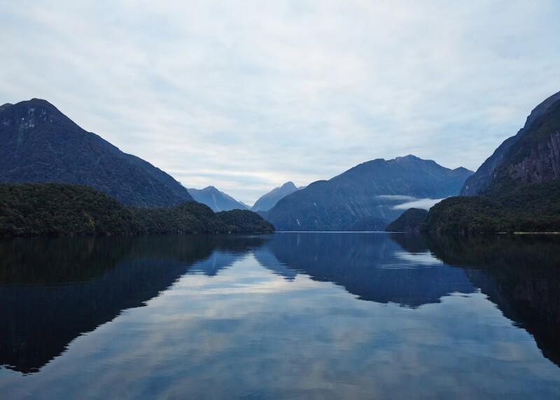 An early morning blue-hued view of Doubtful Sound, with mountains reflecting on water