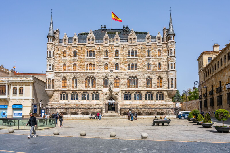 Front of multi-story stone building, Casa Botines, with Gothic turrets and ornate window surrounds, plus Spanish flag at center of roof