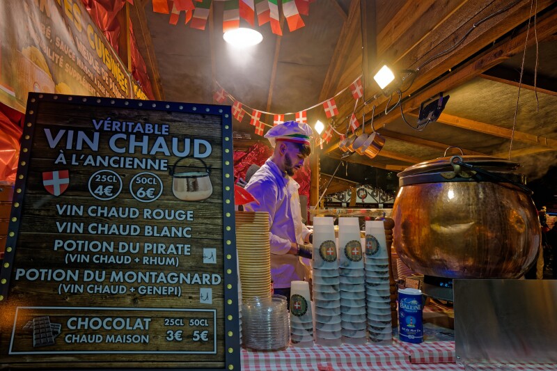 A vendor at the Christmas market in Lyon, France, selling "vin chaud" with a large bronze cauldron and stacks of cups