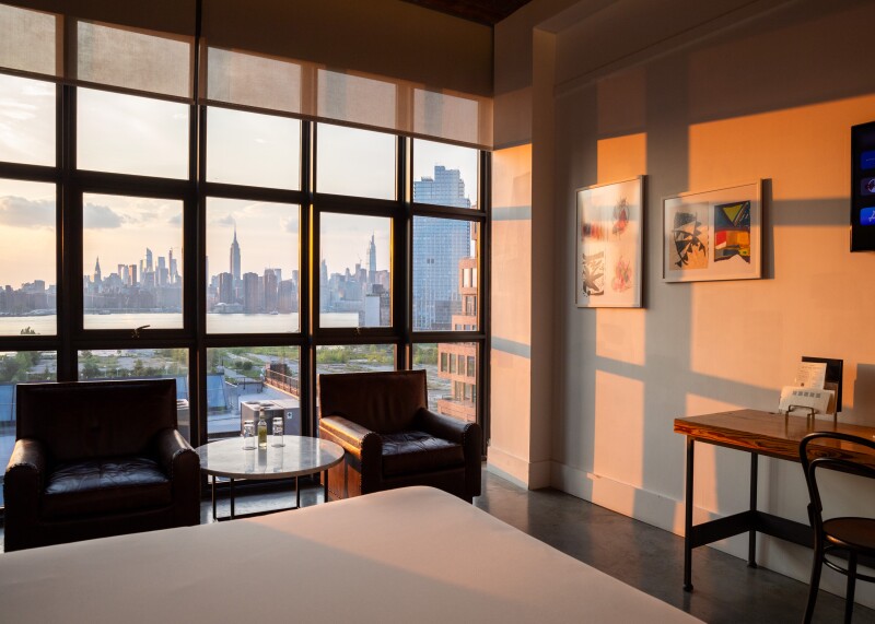 Guest room at the Wythe Hotel, with views of Manhattan skyline through wall of windows