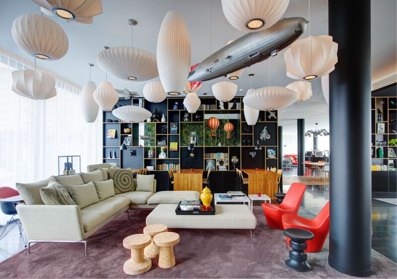Lobby/lounge area of citizenM Paris Charles de Gaulle Airport hotel, with lots of white hanging ceiling lights, a sofa and two red chairs