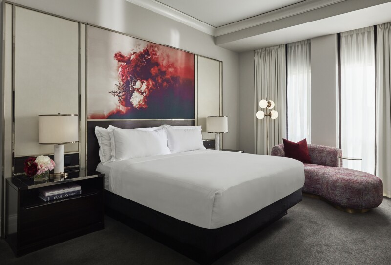 White and gray guest room, with red artwork above bed and chaise longue by tall curtained windows