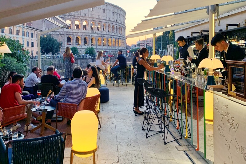 People at tables beside the outdoor Court cocktail bar, with the Colosseum in background