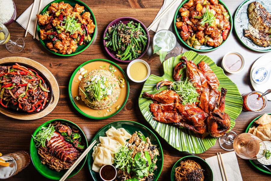 Overhead view of eight plates of different foods on wood tabletop at Beautiful South