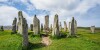 The Calanais Standing Stones situated in something of a circle surrounding by green grass and a blue sky with clouds overhead