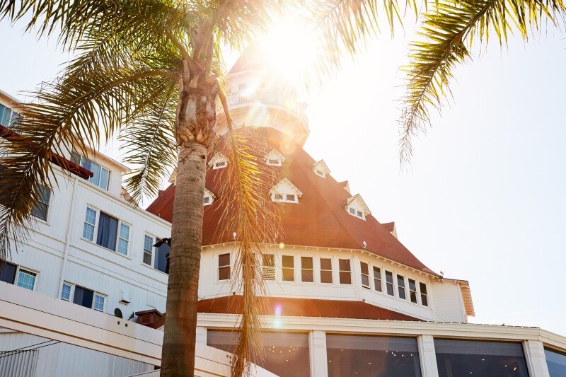 Sun shining from behind the rounded, red peaked roof of Hotel del Coronado