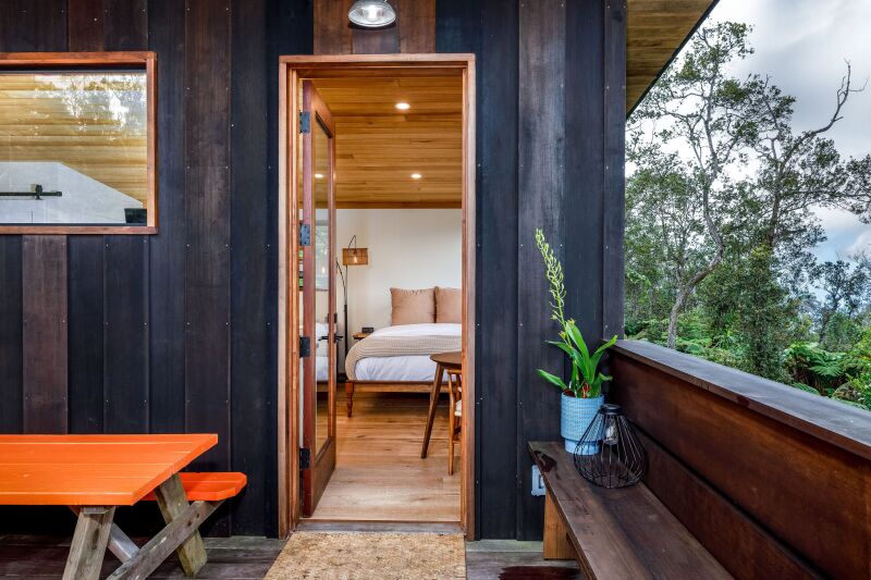 A view into a tiny home through open door, with an orange picnic table on the patio and black wood walls