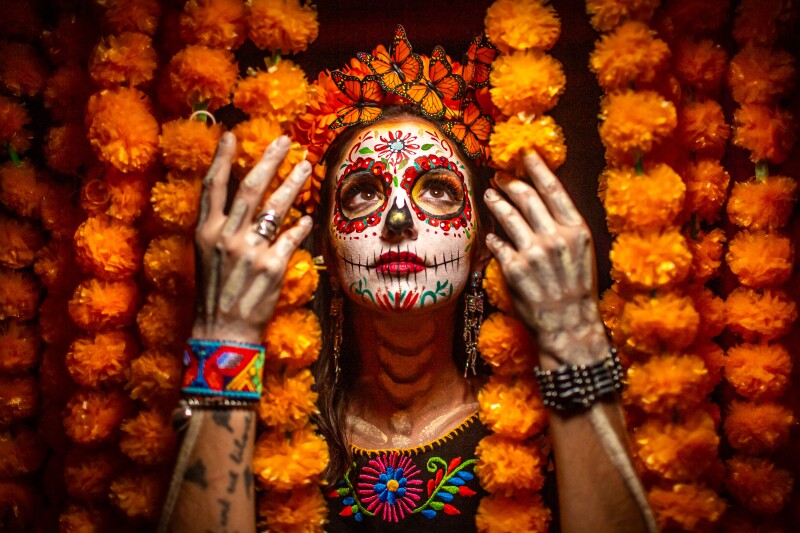 A woman sorrounded by marigolds and wearing Day of the Dead makeup.