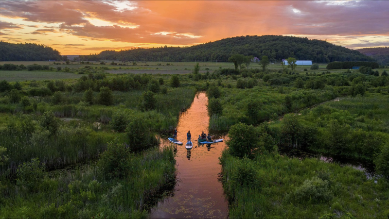 A high view during sunset of people stand up paddle boarding through a marshy waterway at the Eco-Odyssée Nature Park in Quebec.