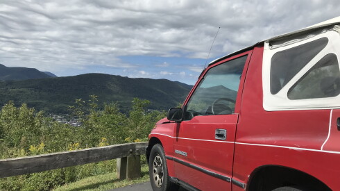 Red car parked at scenic overlook in the Blue Ridge mountains. The view is of green hills and mountains