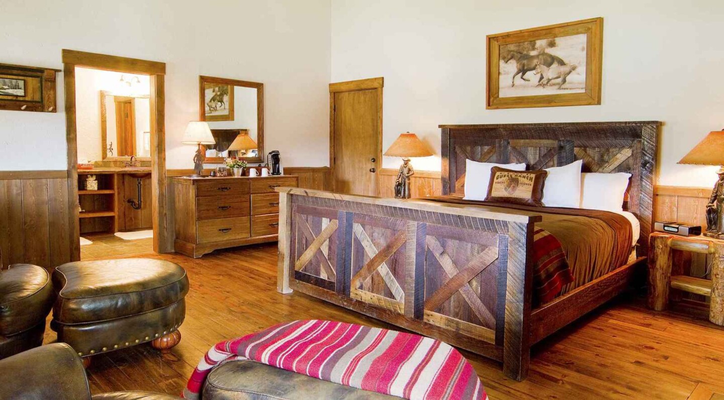 A spacious guest room with wooden floors and bed in a wood frame; above it hangs a painting of running horses