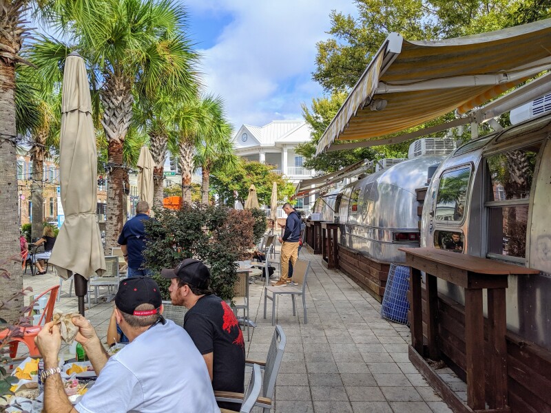 Patrons dine alfresco next to Airstream food trucks under palm trees in downtown Pensacola