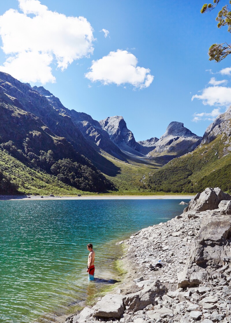 A young boy standing in the shallow blue water of an alpine lake