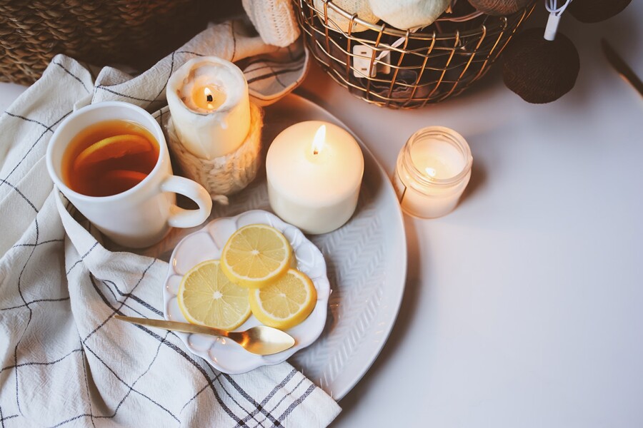 Overhead view of cup of tea and small plate of lemon slices, with 3 short, white lit candles on tabletop