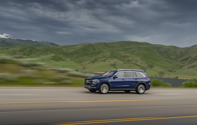 Blue Mercedes-Benz SUV on highway with green hills and cloudy sky in background