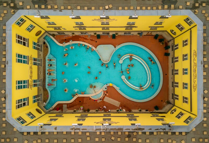 Aerial view of large curvy pool at Szent Lukács Bath, with people in water, surrounded by yellow walls