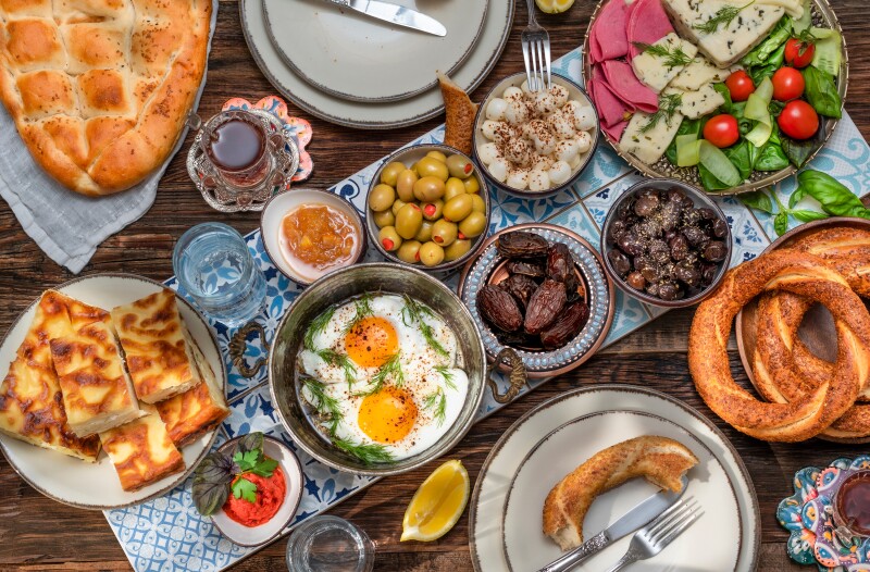 A traditional Turkish breakfast with tomatoes, cucumbers, cheese, butter, eggs, honey, bread, bagels, olives and cups of tea.