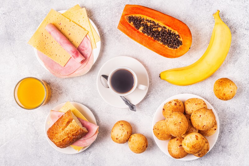 Brazilian breakfast: cheese bread, sandwiches, orange juice, coffee, and fruit.