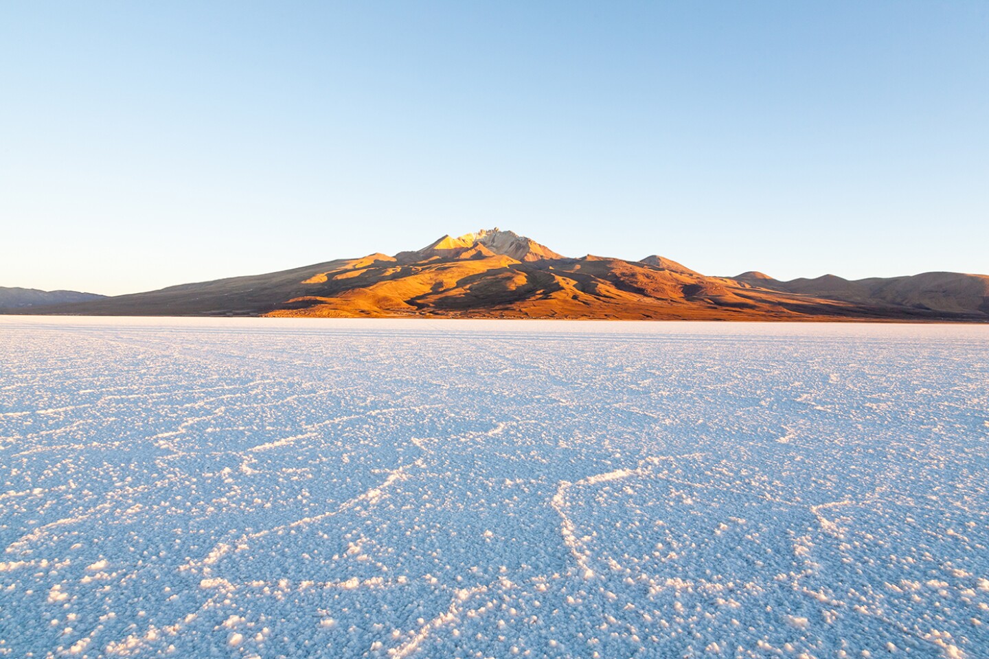 The blue-white salt flats at Salar de Uyuni, Bolivia, with reddish hills in background