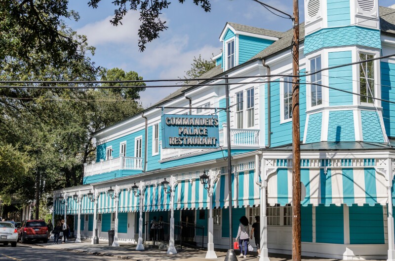 Exterior of Commander's Palace restaurant in a teal building with teal-and-white striped awnings.