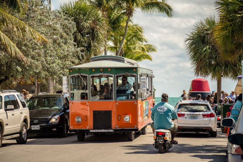 A wheeled trolley drives along with cars on a street in Key West, Florida. The tropical city is a popular tourist destination with over 2 million yearly visitors.