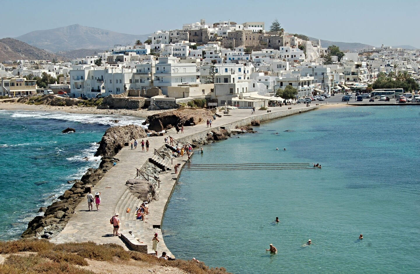 A village with white buildings behind a long walkway stretching between two bodies of water