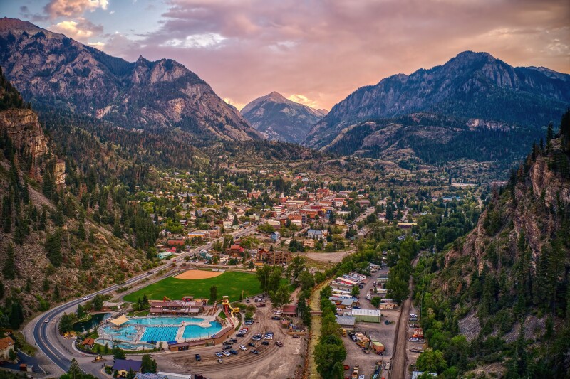Aerial view of small town with a complex of pools in foreground surrounded by mountains under a pink-cloud sky