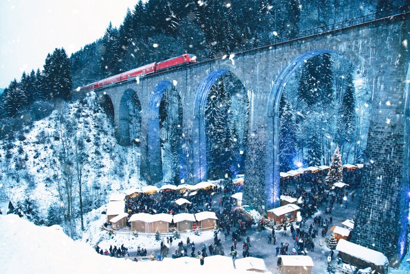 The Ravenna Gorge Christmas Market, with snow, beneath railroad bridge carrying red train