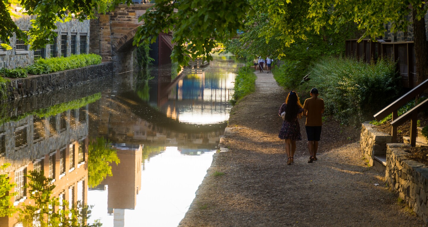 Two people walking away from the camera down a path alongside a canal in Georgetown, Washington D.C.