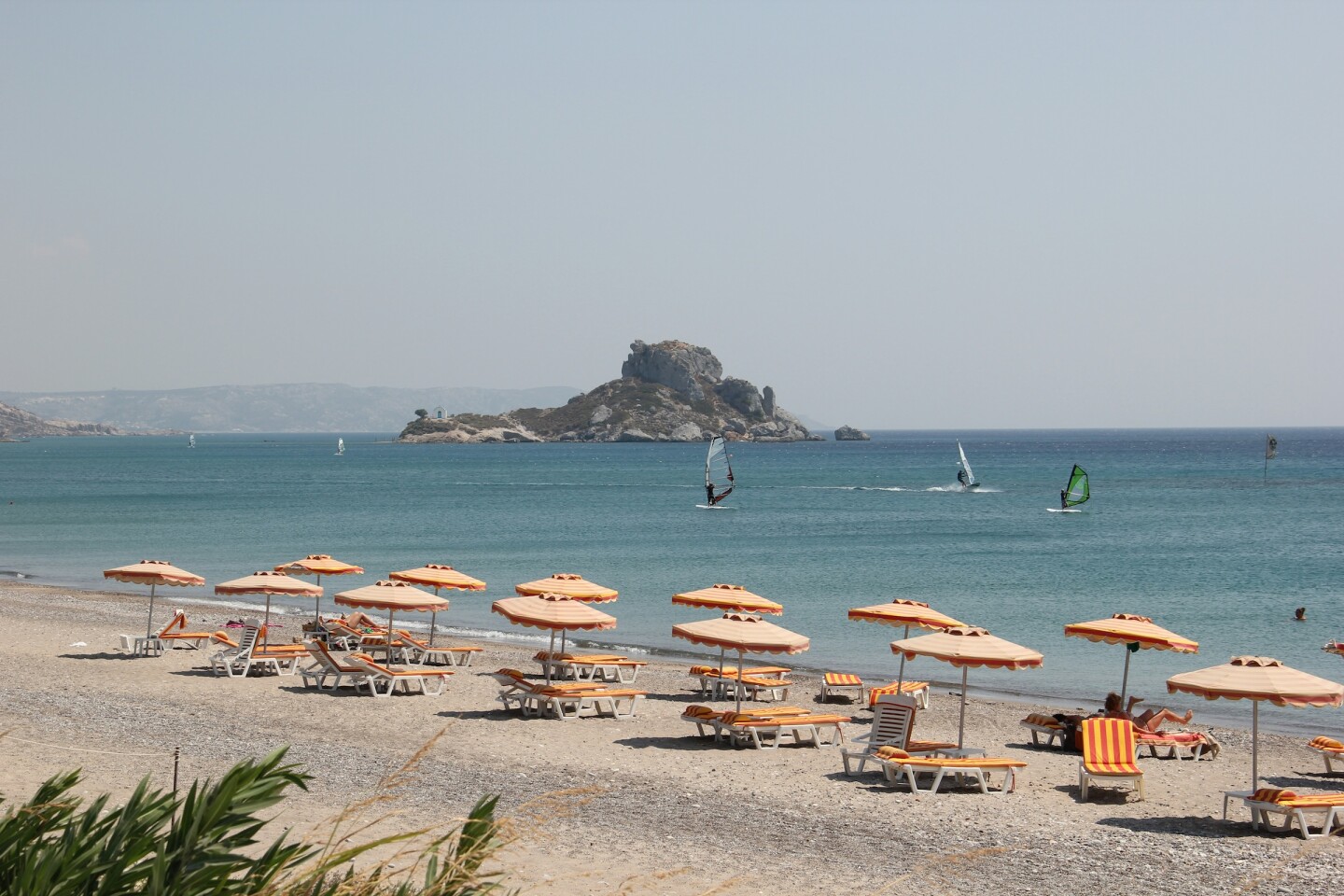 Orange umbrellas on a beach with a small island in the background 