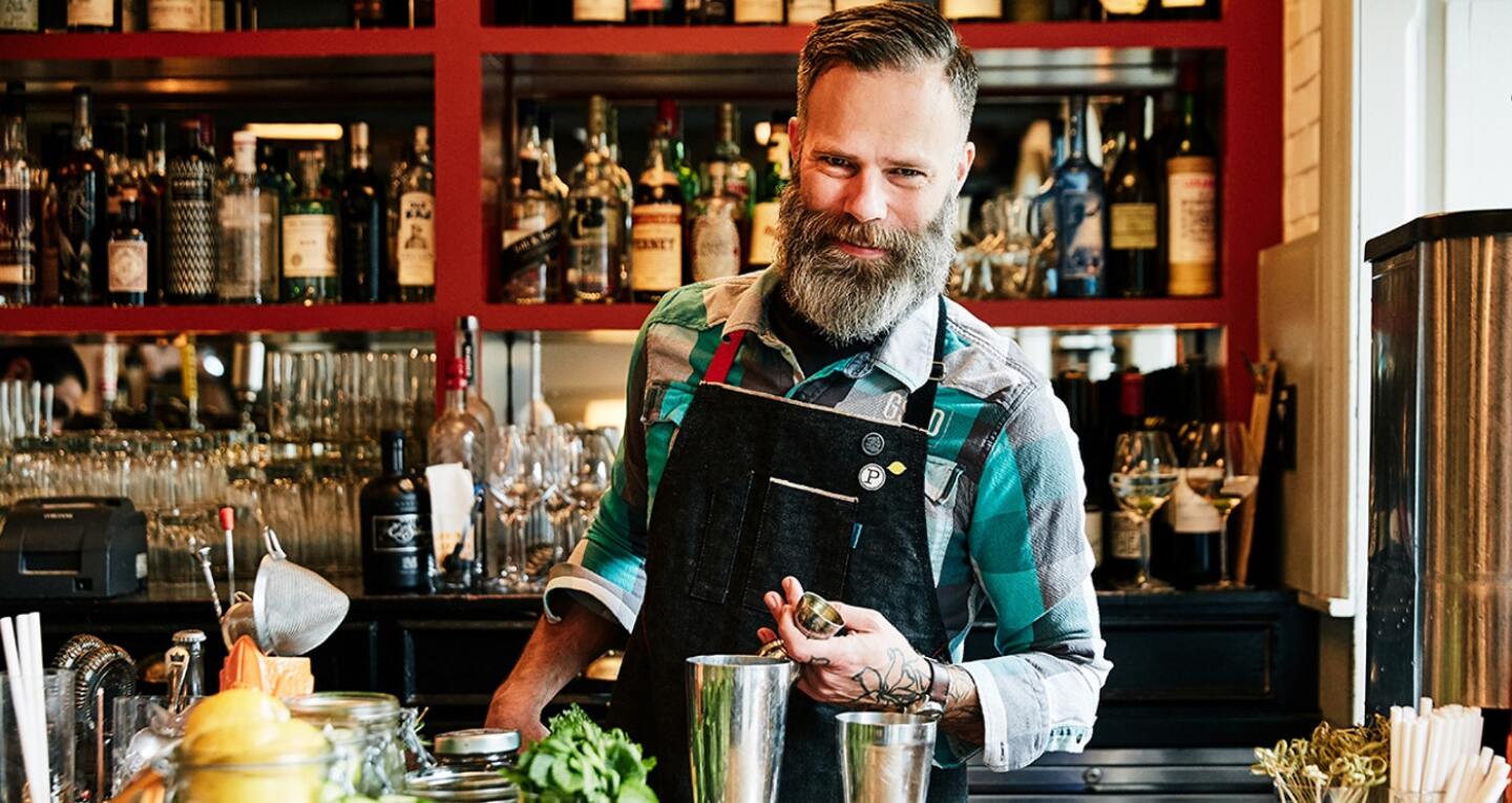 A man in a thick beards tends the bar.