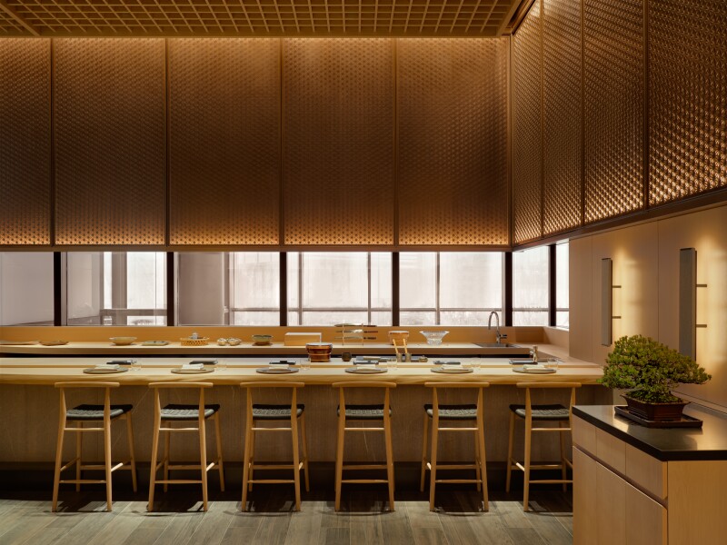 Iigura sushi restaurant, with long counter made of hinoki wood and six tall chairs and place settings on it; bonsai tree at right