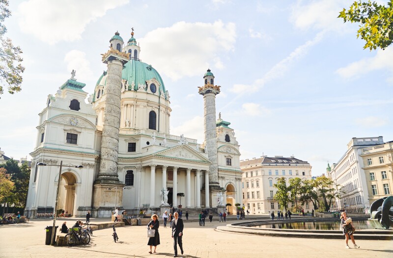 Exterior of the white Karlskirche church in Vienna, with blue dome, and circular plaza in foreground