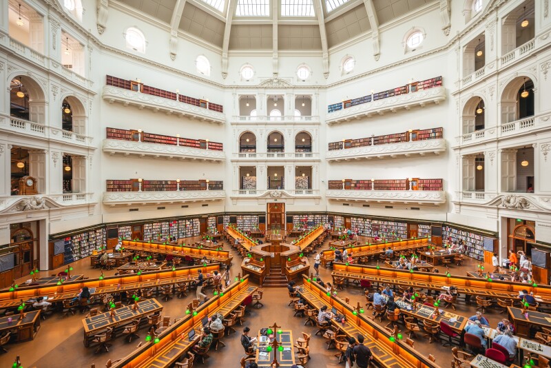 Rows of desks in spoke formation at Melbourne's State Library Victoria, with curved white wall and edge of glass dome in background
