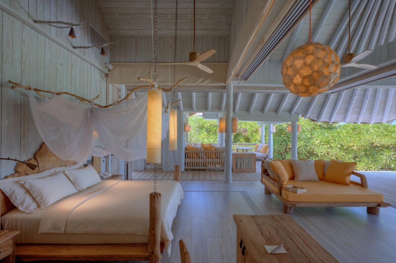 White bedroom at Soneva Secret, with wood beam ceilings, hanging fans, and large orange daybed