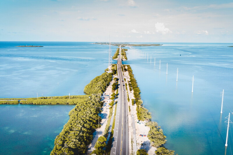Aerial view of long highway crossing water, with greenery on each side
