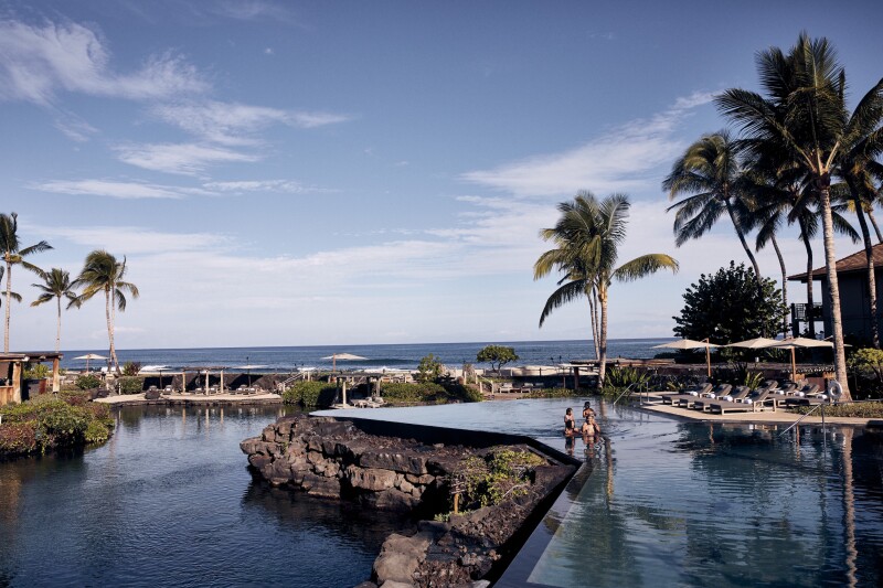 A group of people wading in Four Seasons Resort Hualalai's swimmable King's Pond, which is also a marine reserve